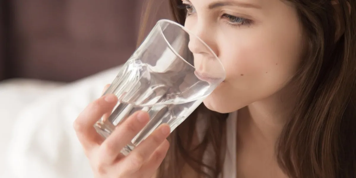 attractive young dehydrated woman feeling thirsty, holding glass and drinking pure mineral water every morning after waking up, good habits for healthy way of life, dehydration concept, close up view