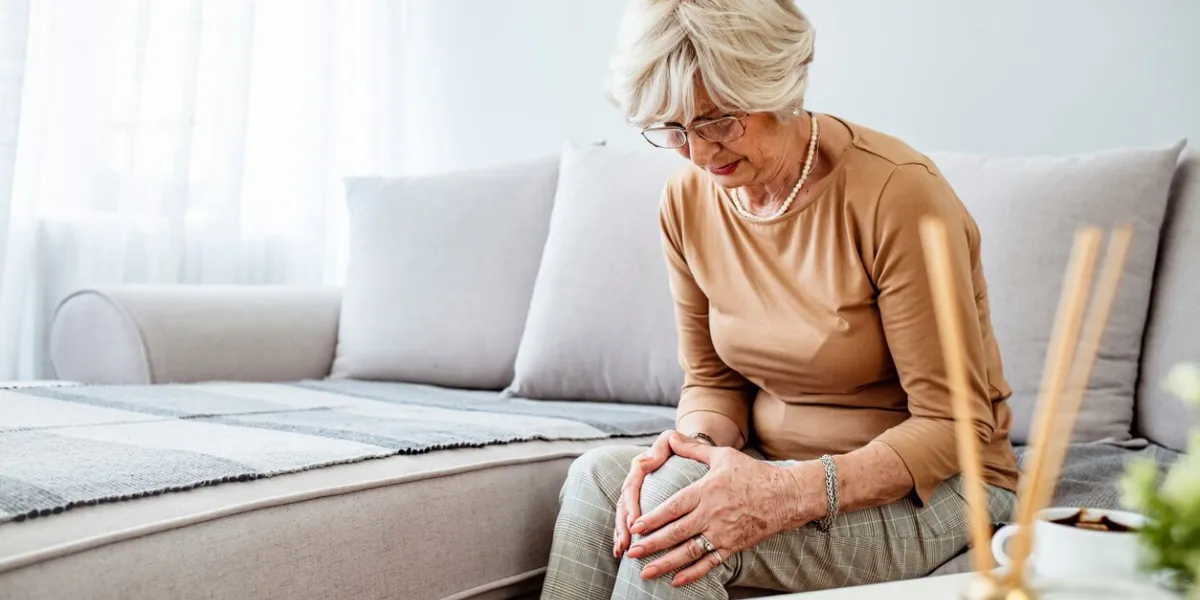 old age, health problem and people concept - senior woman suffering from pain in leg at home elderly woman suffering from pain in knee at home