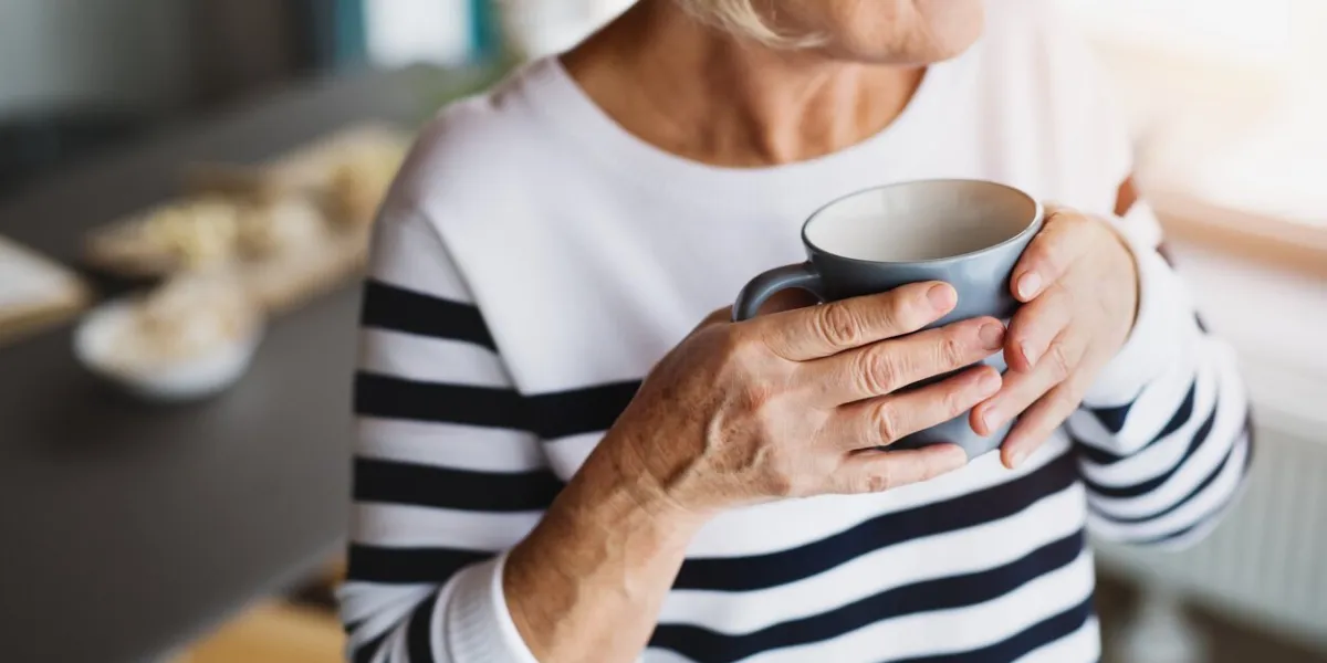 unrecognizable senior woman in the kitchen an old woman inside the house, holding a cup of coffee