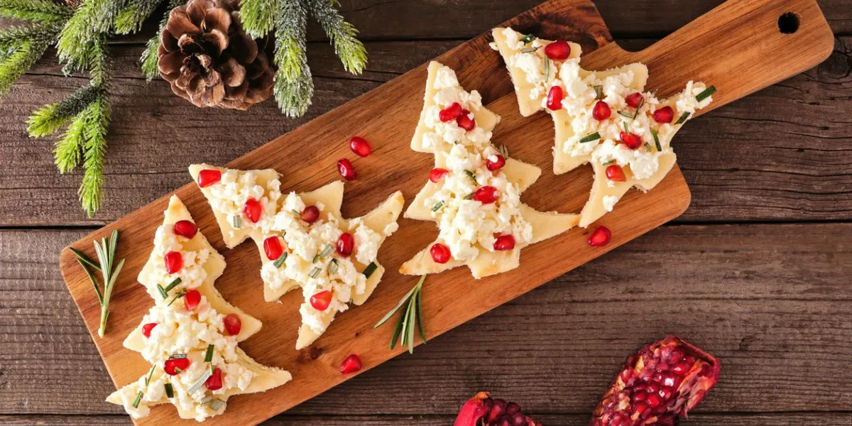christmas tree shaped appetizers with feta cheese, pomegranate and rosemary overhead view on a serving board against wood