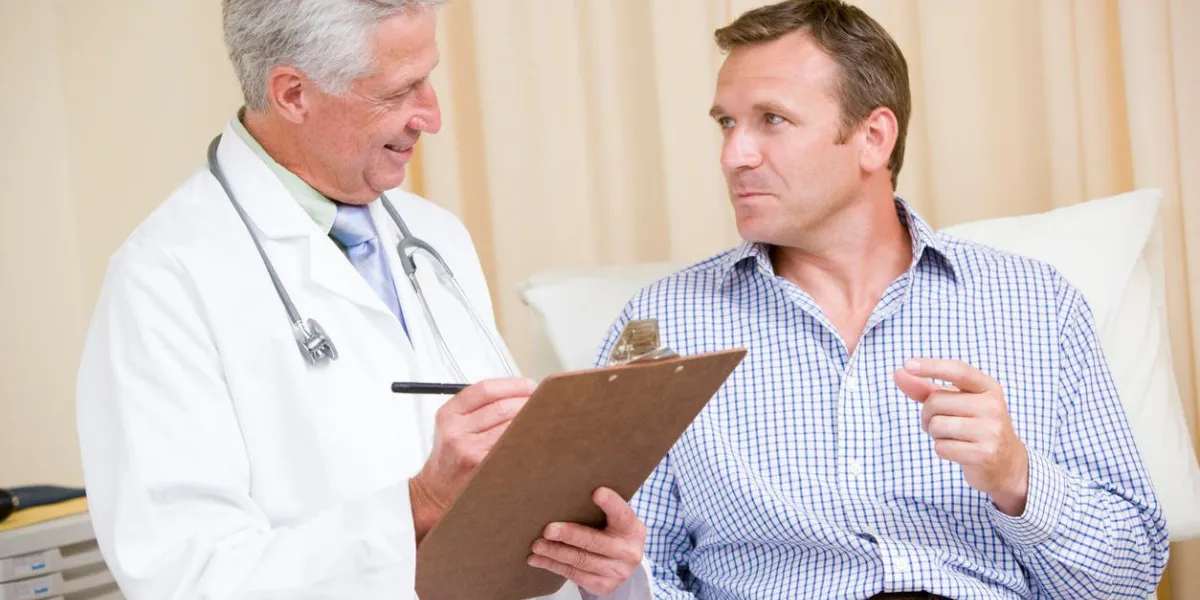 doctor writing on clipboard while giving man checkup in exam room