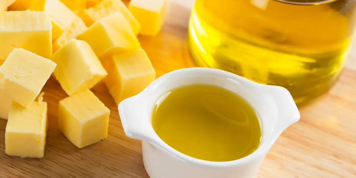 olive oil in small glass container with bottle of oil and cubes of butter