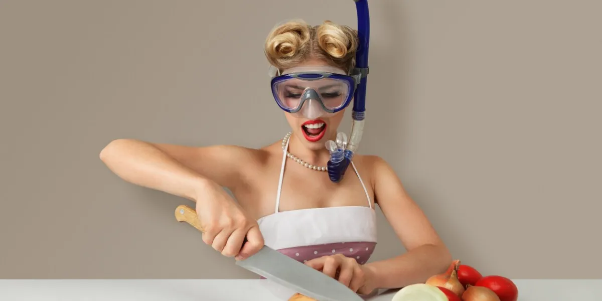 young blonde woman cutting onion in diving scuba mask for protect eyes
