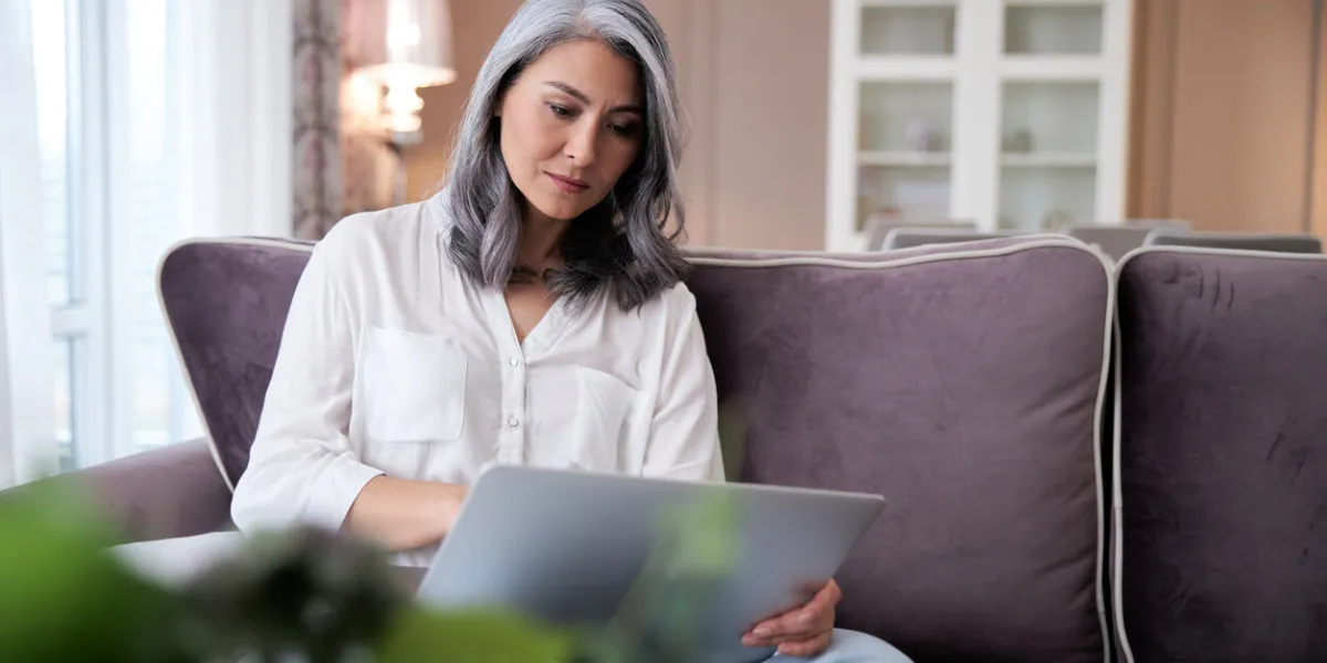 adult thoughtful woman using a laptop while sitting on a sofa