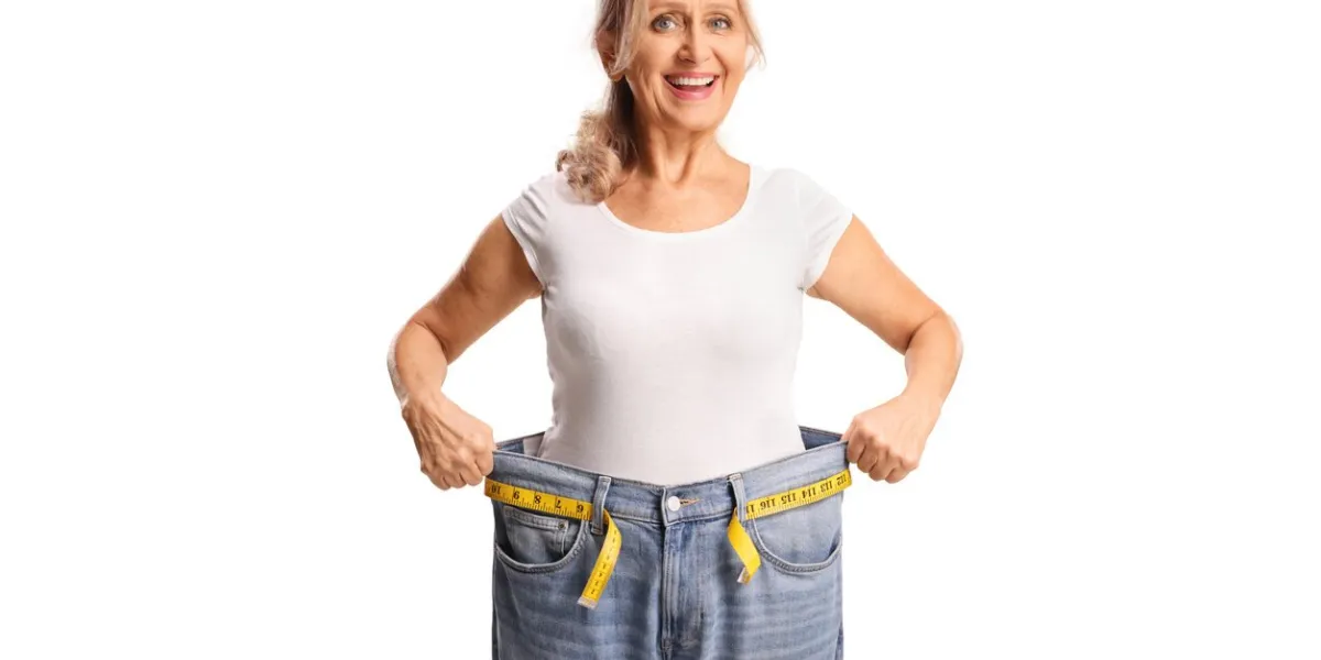 happy middle aged woman trying on a pair of jeans, weight loss concept isolated on white background