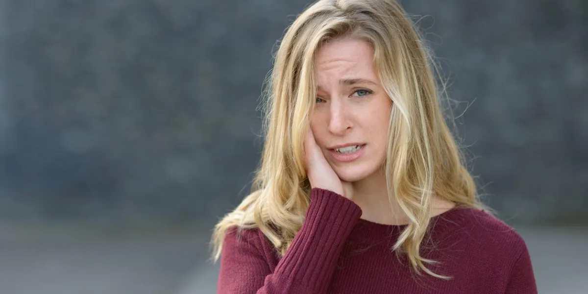 sad young woman with a melancholy expression standing holding her hand to her cheek as she looks at the camera with copy space
