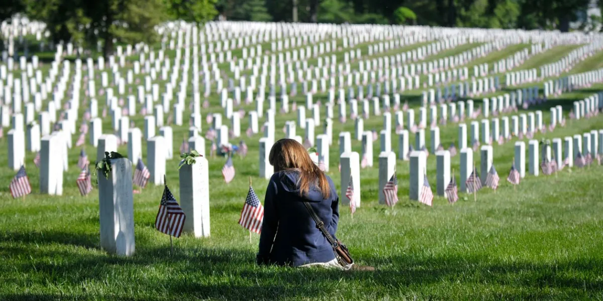 arlington, va usa - may 27, 2013  a young woman sits beside a grave marker at arlington national cemetery on memorial day