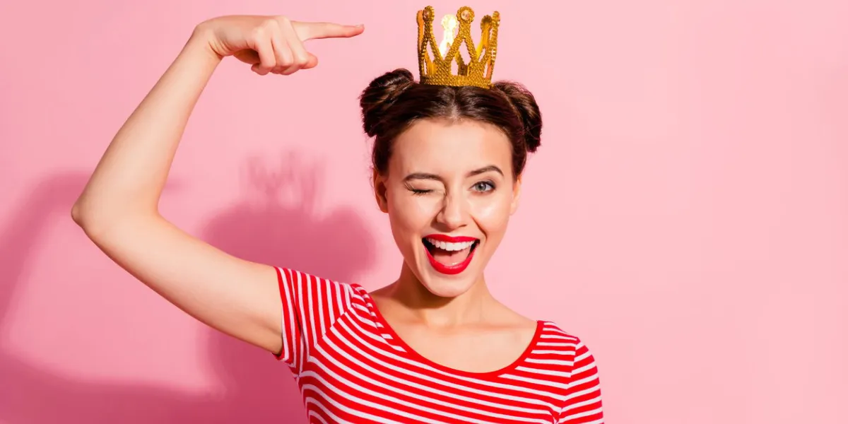 close-up portrait of her she nice cute attractive lovely winsome gorgeous cheerful cheery glad flirty girl wearing striped t-shirt showing cool gold diadem isolated over pink pastel background