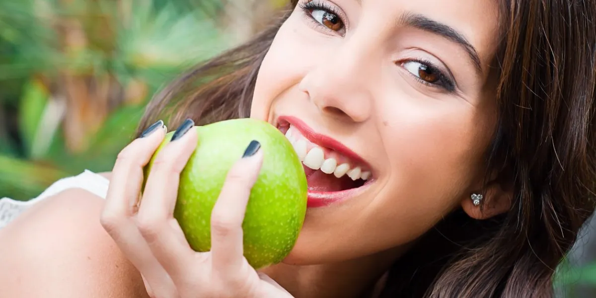 young woman face eating a green apple and looking at the camera with a smile