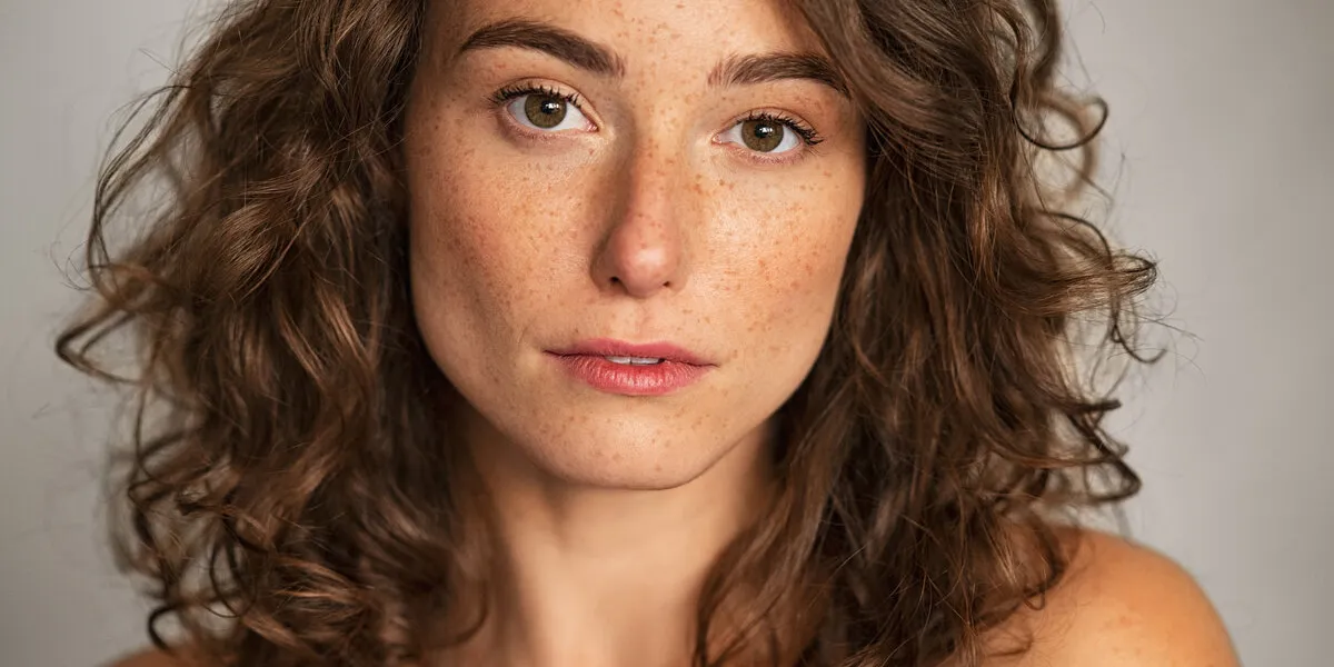 close up face of beautiful woman with healthy natural skin looking at camera portrait of young woman with nude shoulder portrait of sensual girl with freckles isolated against grey wall background