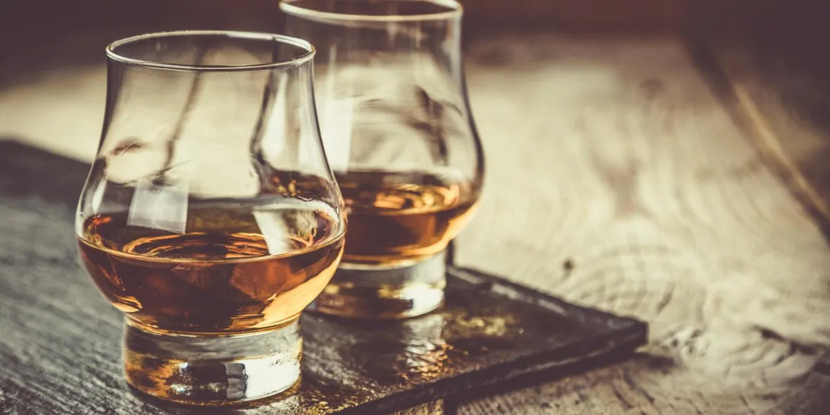 whiskey with ice in glasses, rustic wood background, copy space