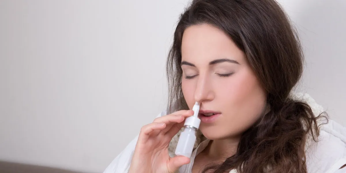 jeune femme à l'aide de spray nasal dans son salon