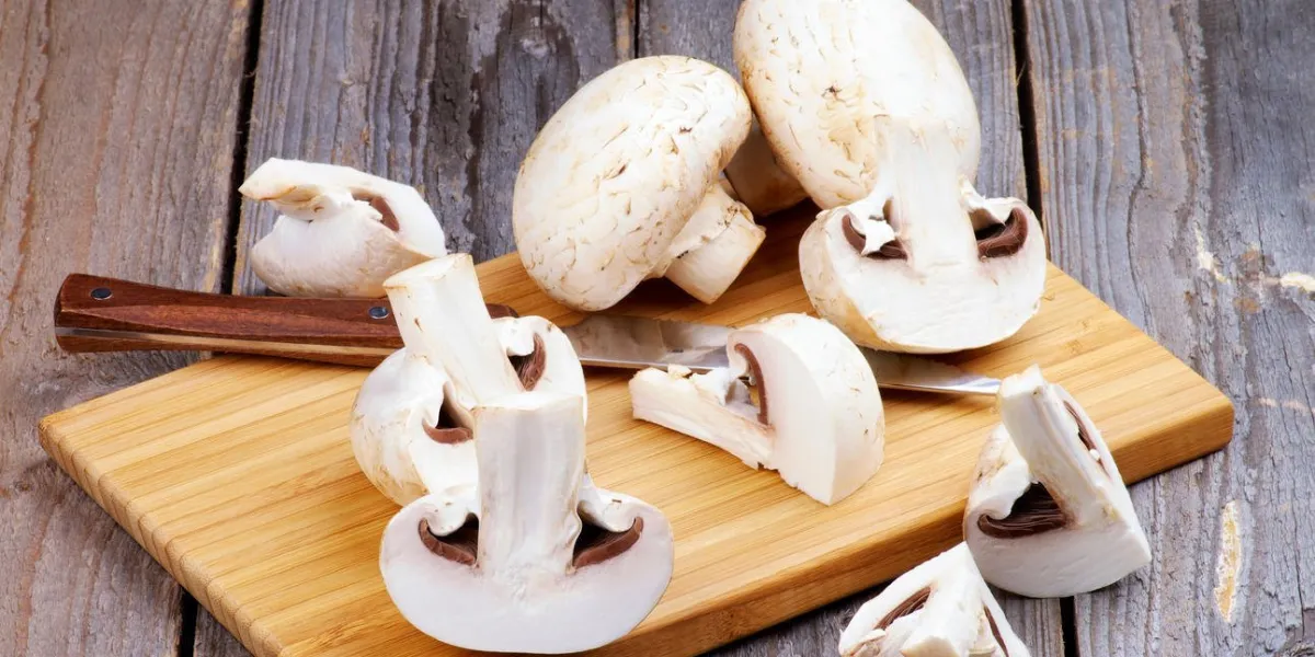 champignons entiers crus et tranches avec couteau de cuisine sur une planche à découper en bois closeup sur fond en bois