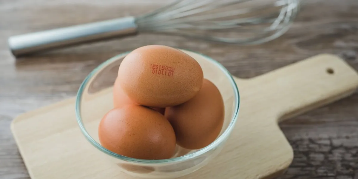 code numbers printed in egg fresh eggs into glass bowl on wooden board on rustic table and beater