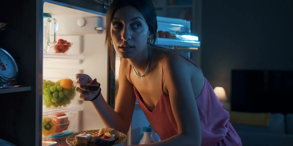 hungry woman looking in the fridge and eating delicious pastries at night, she is breaking her diet