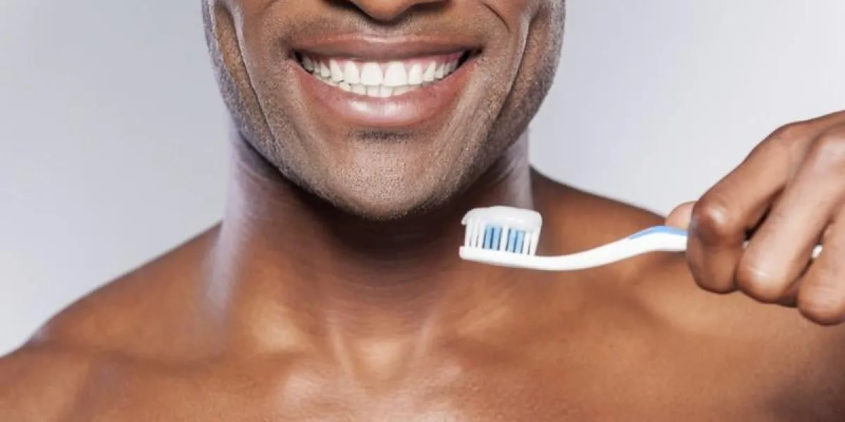 homme avec brosse à dents recadrée image de jeune homme africain torse nu tenant une brosse à dents avec du dentifrice et souriant en se tenant debout sur fond gris