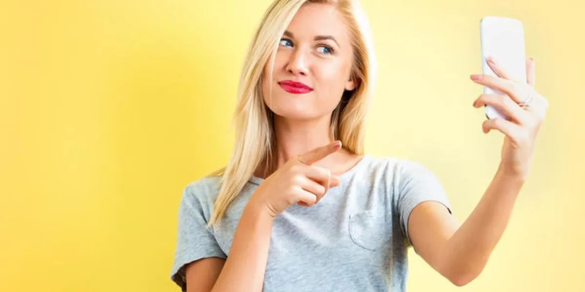 young woman taking a selfie on a yellow background