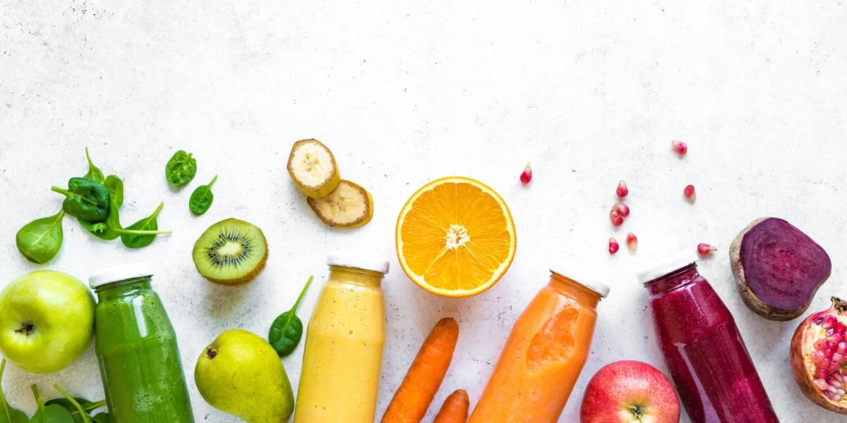 various smoothies or juices in bottles and ingredients on white, healthy diet detox vegan clean food concept, top view, copy space