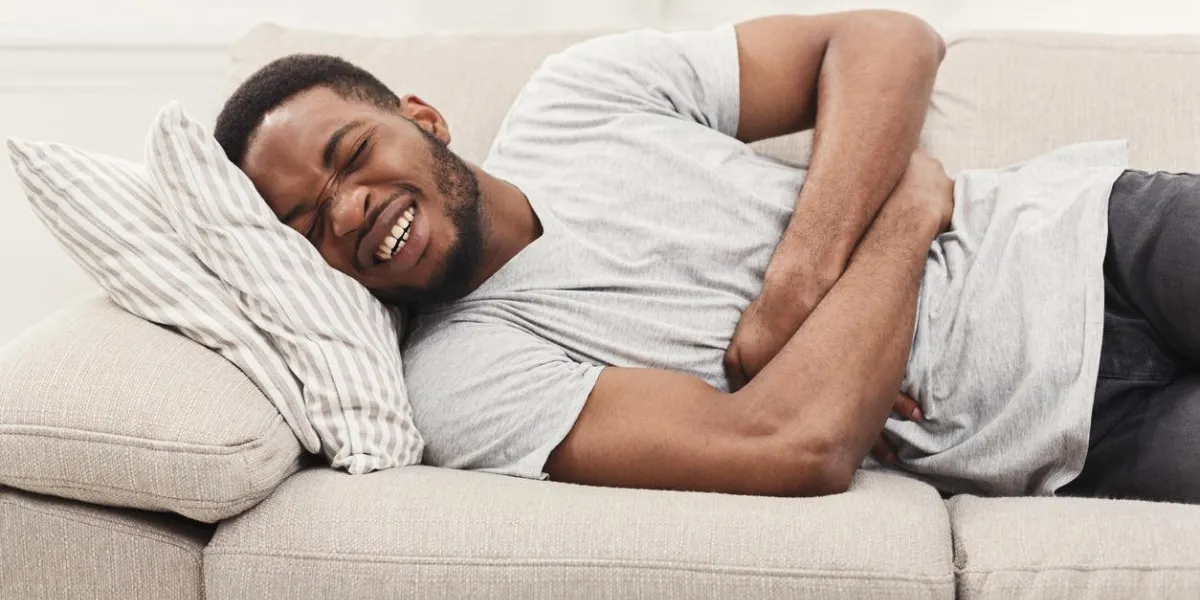 handsome young african-american man suffering from stomach ache while lying on sofa at home