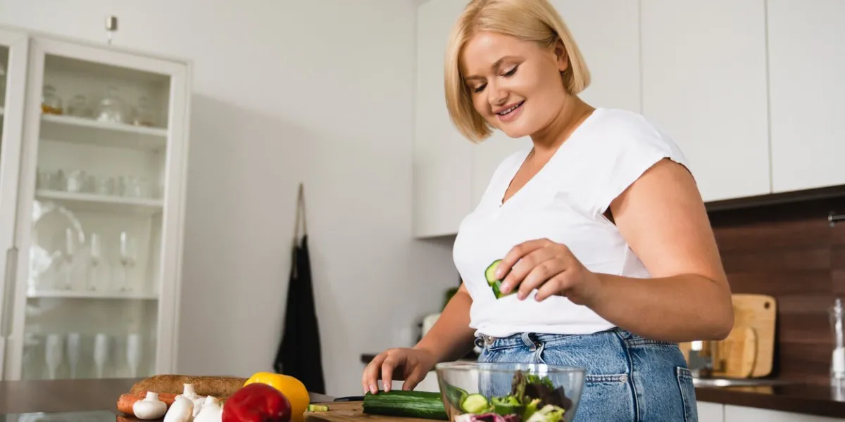 young caucasian plump plus size woman cooking making salad, healthy food, dieting, counting calories, preparing dinner lunch at home kitchen