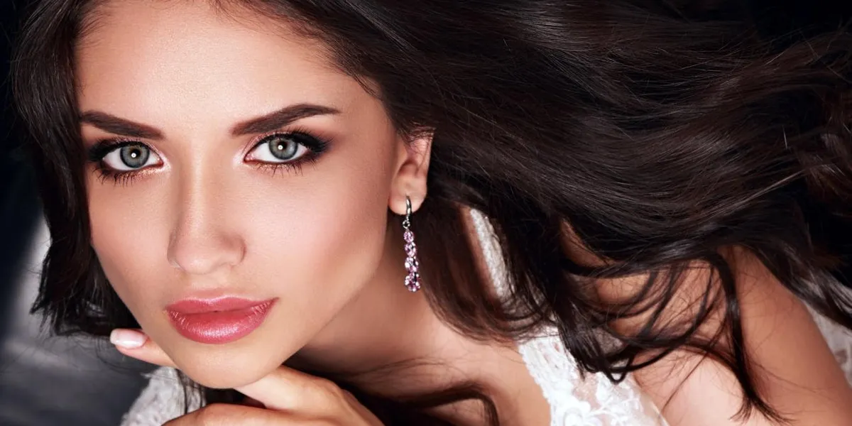 belle femme de maquillage avec le rouge à lèvres rose et long cheveux bouclés qui posent à la mode boucles d'oreilles closeup portrait