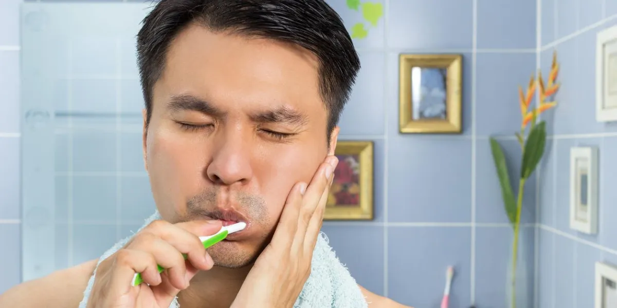 asian handsome man with toothache while brushing the teeth in blue bathroom