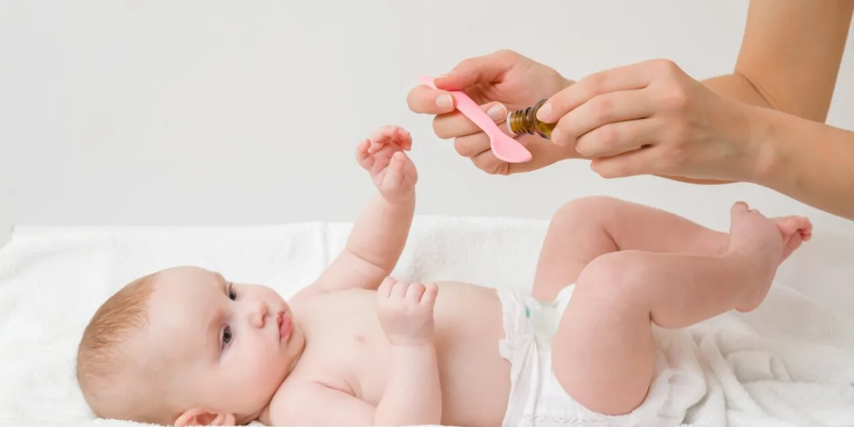 young mother hands holding pink plastic spoon and bottle of medicines infant lying down on changing table and receiving vitamins side view close up
