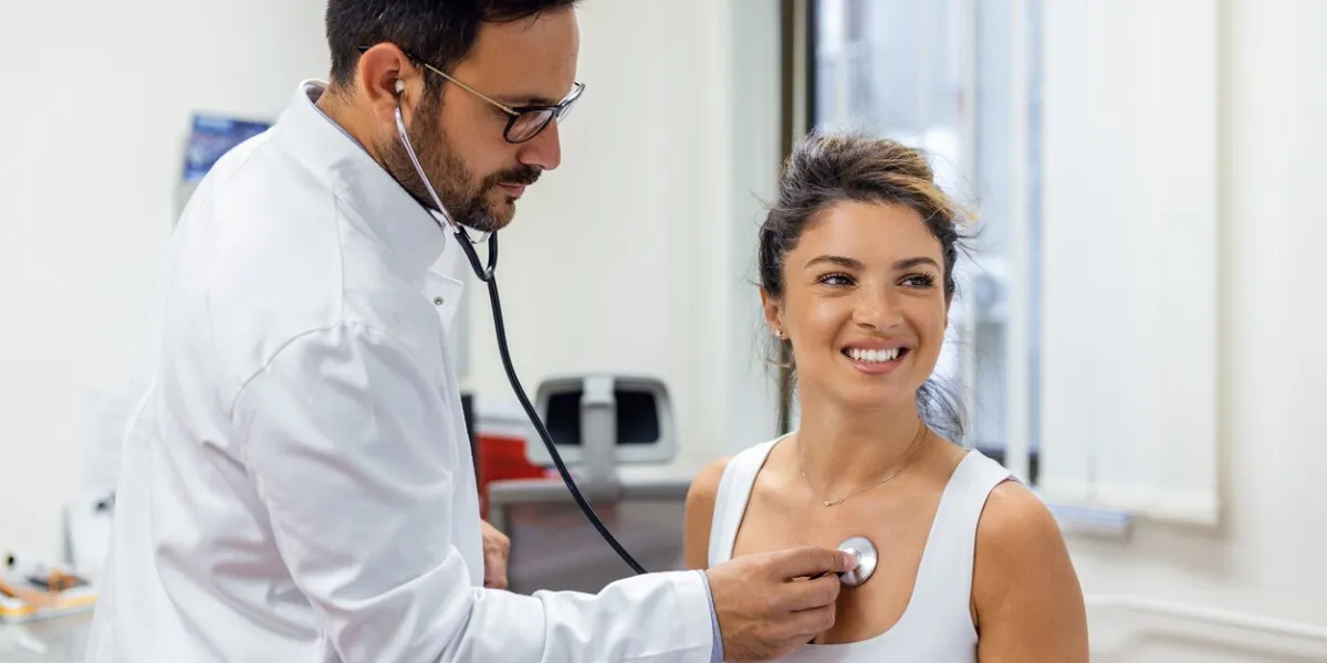 young doctor listen to female patient heart chest with stethoscope at clinic meeting man gp checkup examine woman client with phonendoscope healthcare concept