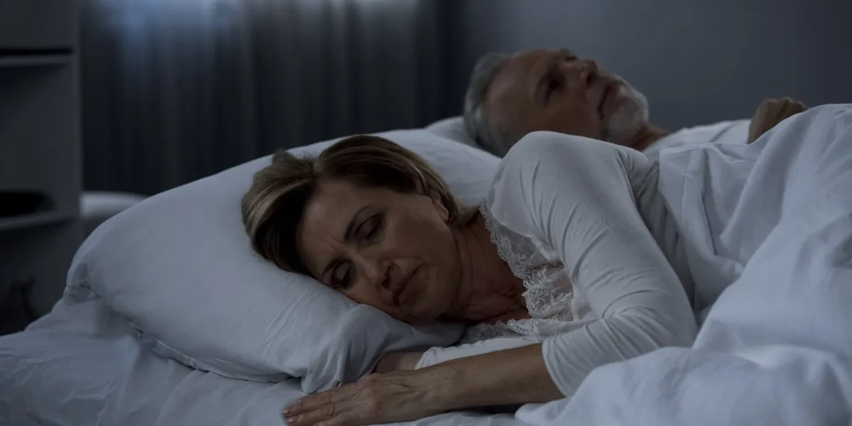 aging husband and wife lying in bed awake, lady turned back to man, low potency