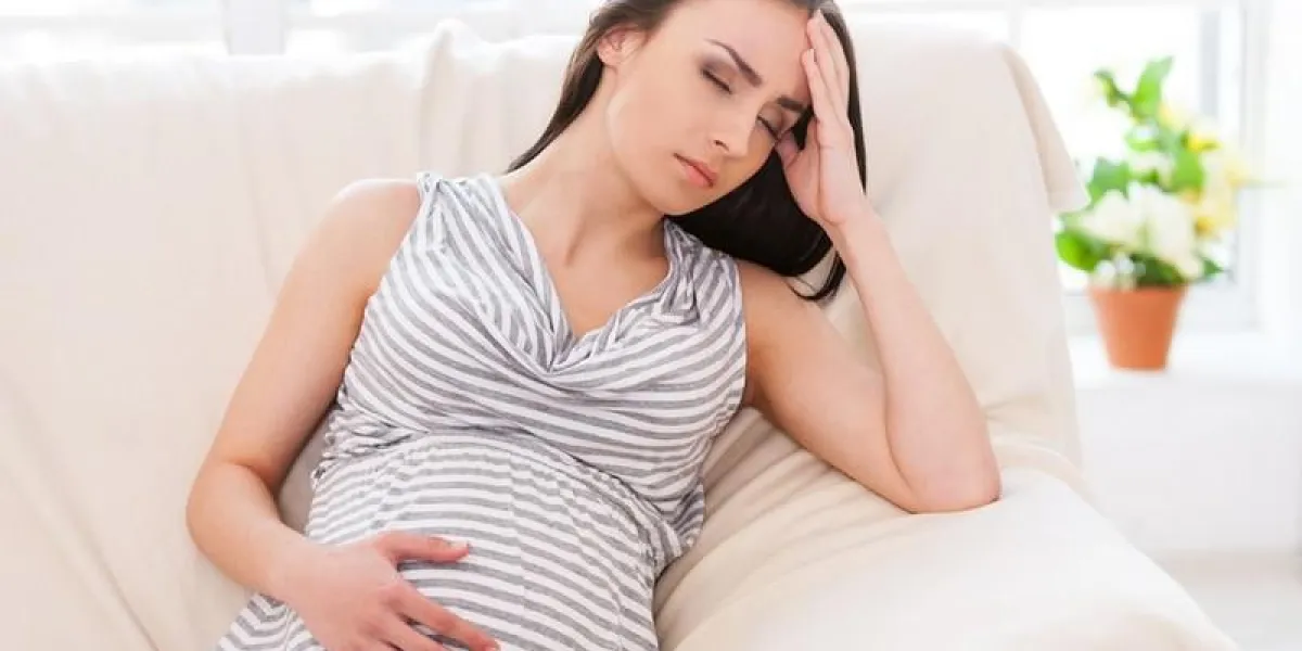 femme enceinte déprimée tenant la main sur la tête et garder les yeux fermés tout en étant assis sur un canapé