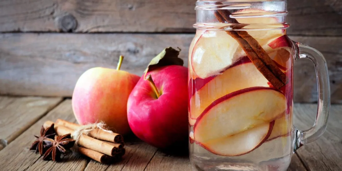 eau de détox à thème automne avec pomme, cannelle et poire rouge dans un bocal de maçon sur un fond de bois rustique