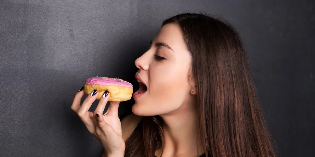 jeune, jolie fille mangeant un beignet, tient un beignet dans sa main devant la bouche