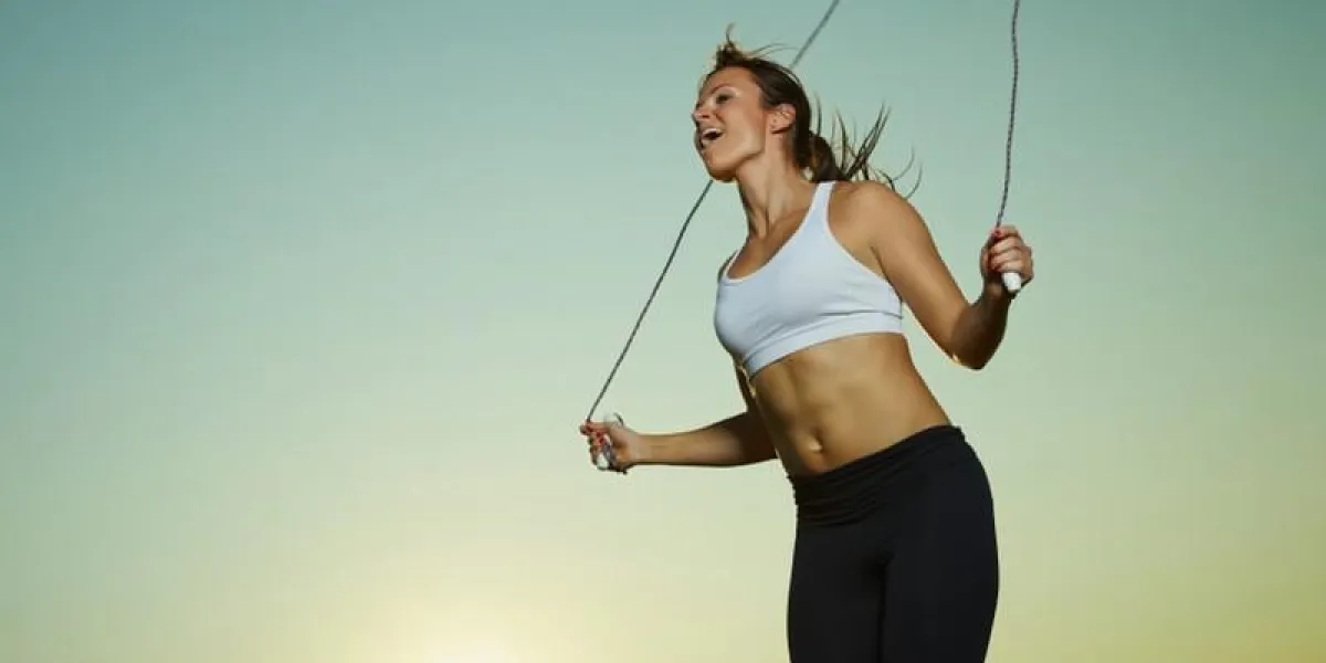 femme jeune de remise en forme a utilisé une corde à sauter, le soleil et le ciel sur fond, copie espace