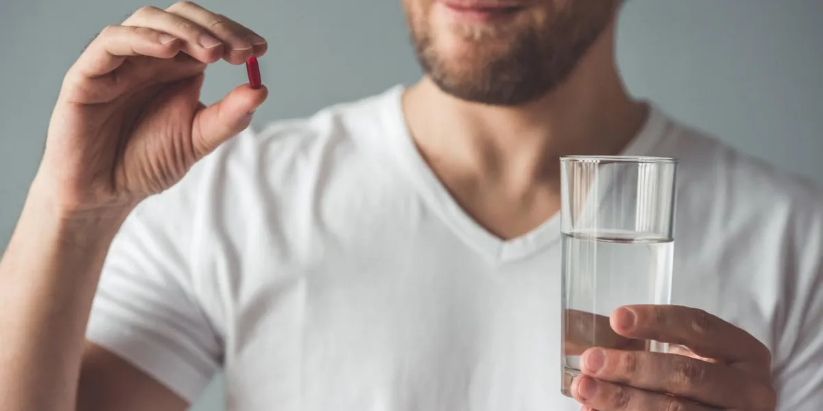 image recadrée de bel homme tient une pilule et un verre d'eau, sur fond gris
