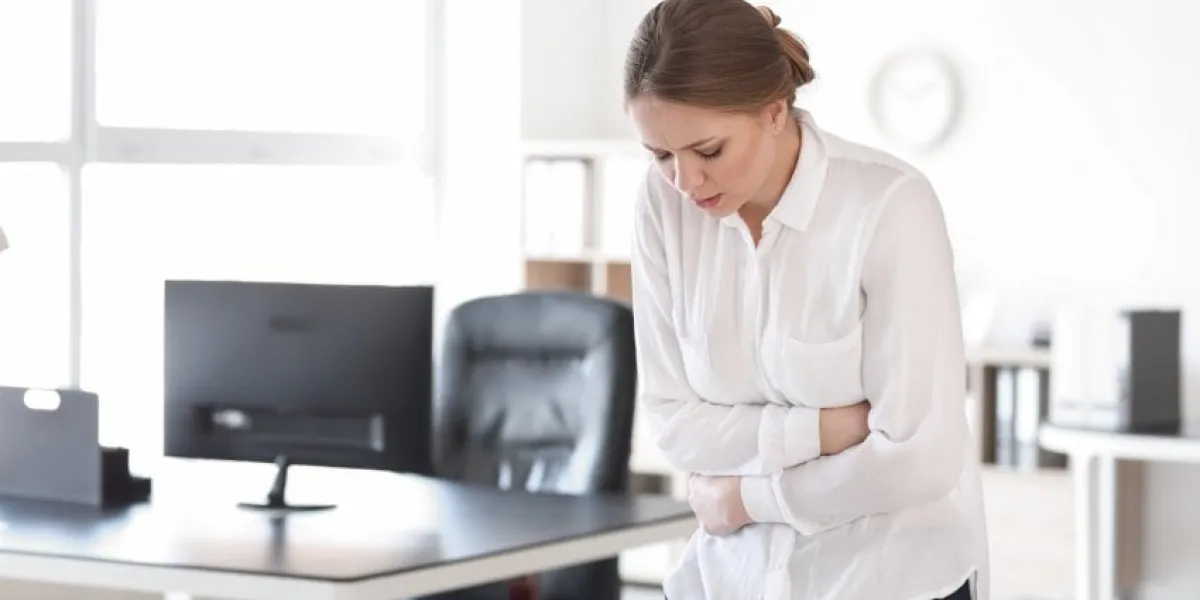 young woman suffering from stomachache in office