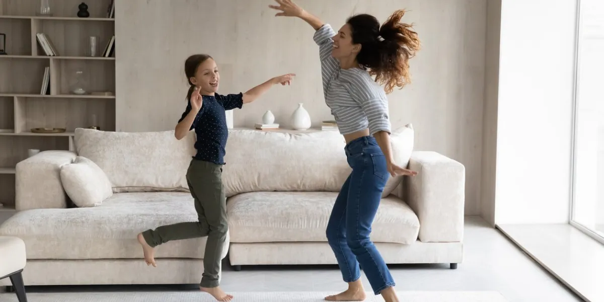 excited active mom and happy daughter kid having fun, going wild, dancing to music in living room, jumping on floor, practicing exercises, moving bodies, listening to radio home activity concept