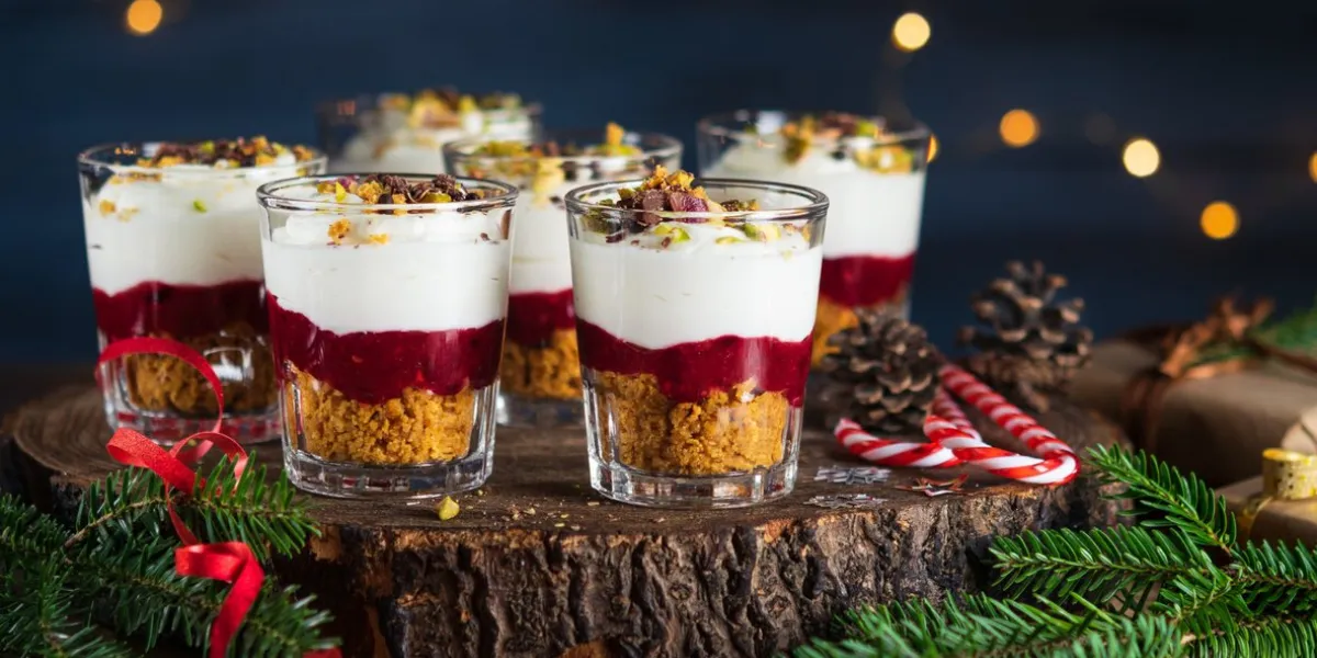 trifle red fruits sauce, cream cheese, cookies crumbs layered dessert in glasses on dark blue background, garland lights bokeh, christmas decoration new year, christmas holidays background concept
