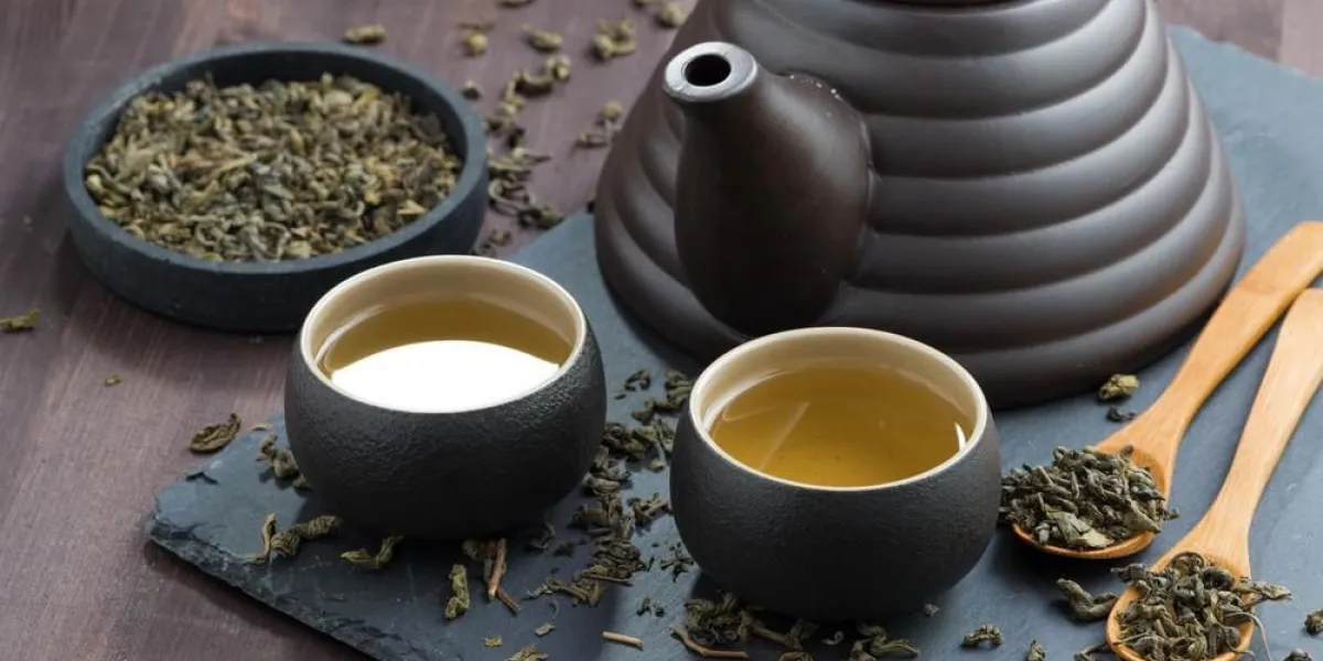 théière et tasses avec du thé vert frais sur une table en bois, gros plan