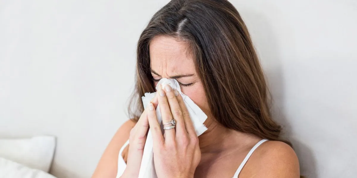 pregnant woman sneezing with tissue on mouth in bedroom