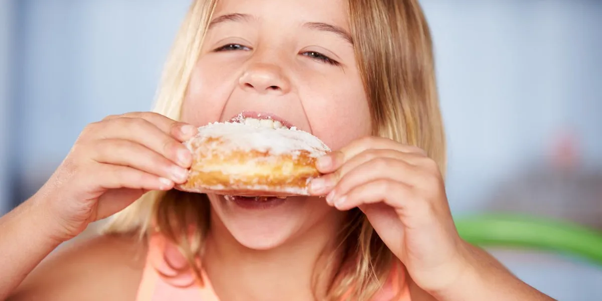 jeune fille assise à table, manger des beignets sucrés