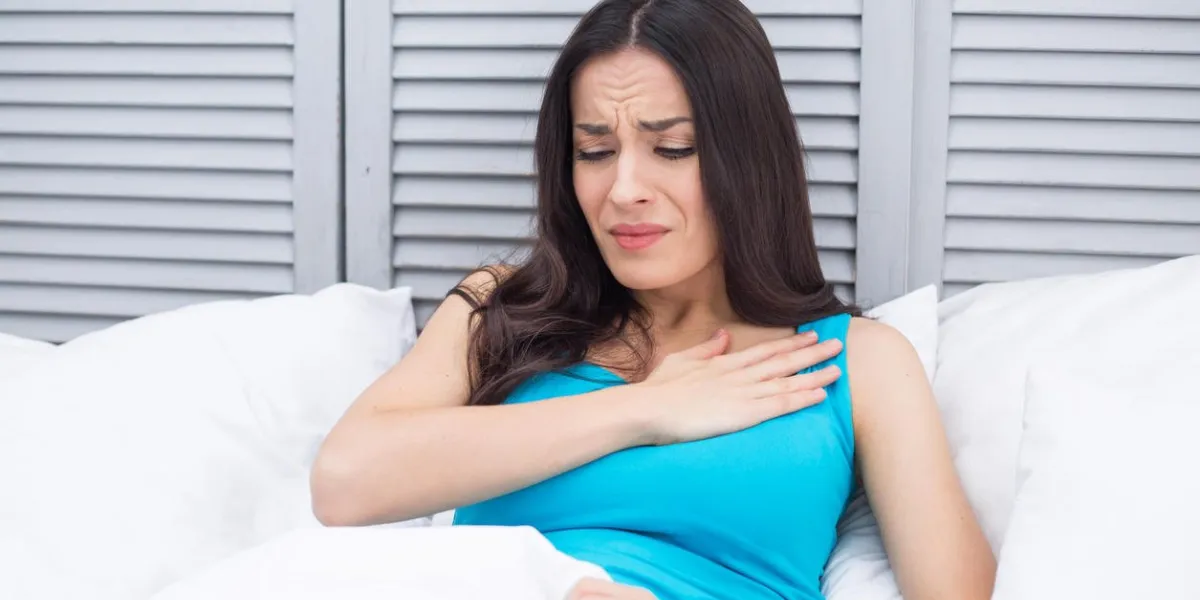 severe pain in the heart young woman lying in bed at home holding a hand to her chest by a sharp pain in heart