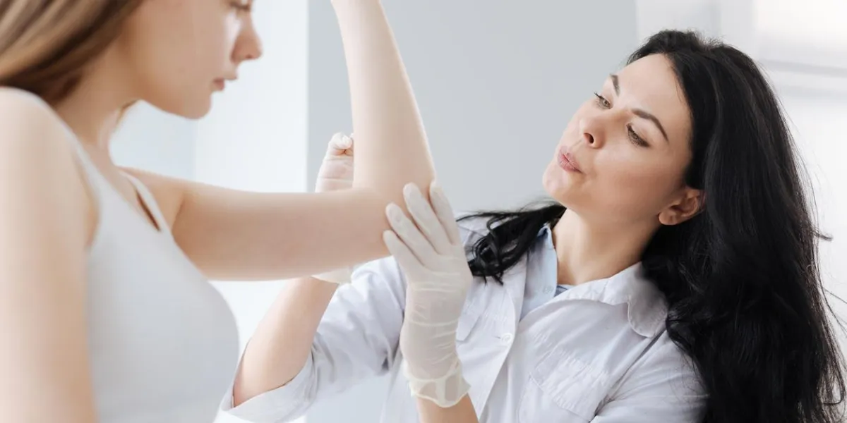 stilling pain charismatic experienced involved medical specialist working in the clinic and enjoying appointment while disinfecting injury and blowing on the arm of the patient