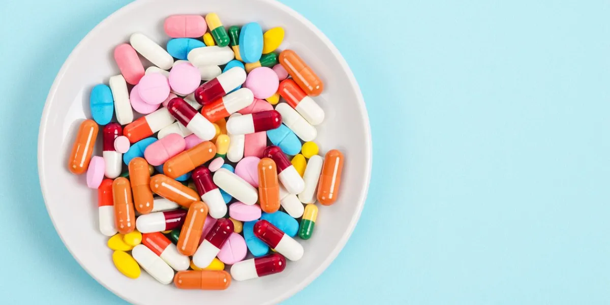 a top view of colourful medicine pills and capsules in white plate on blue background copy space for the ads