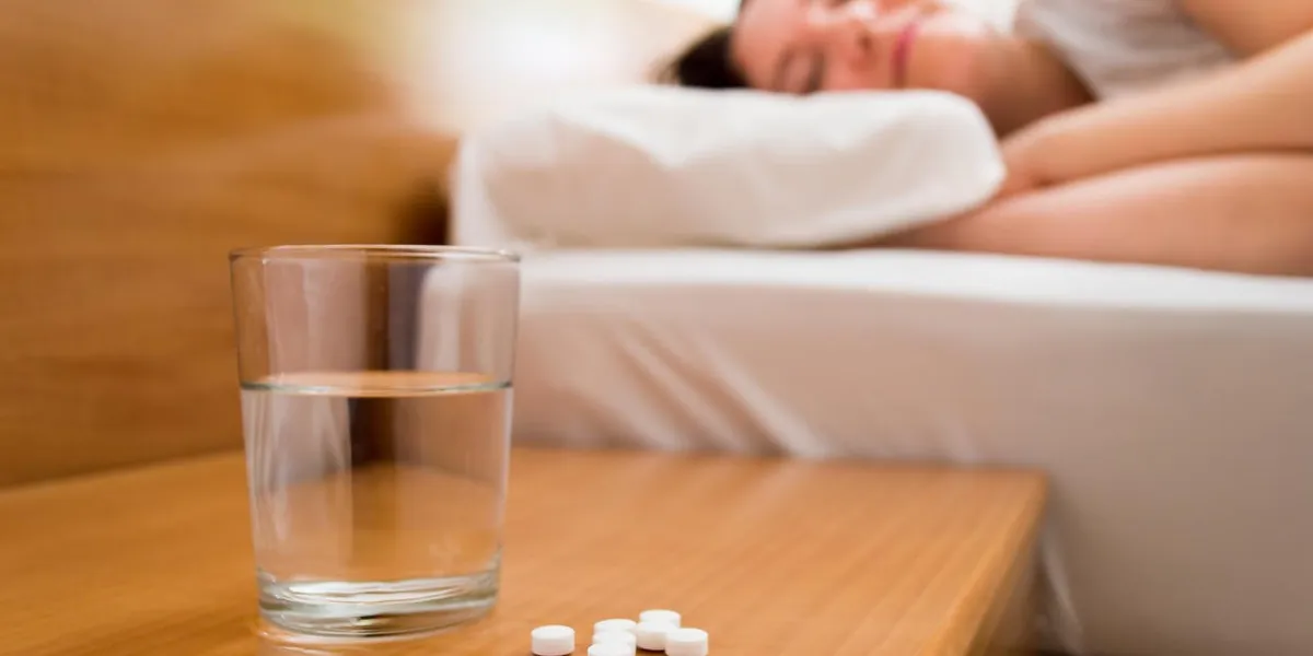 gros plan de médicaments avec le verre d'eau sur la table de chevet avec une femme qui dort sur le lit en arrière-plan