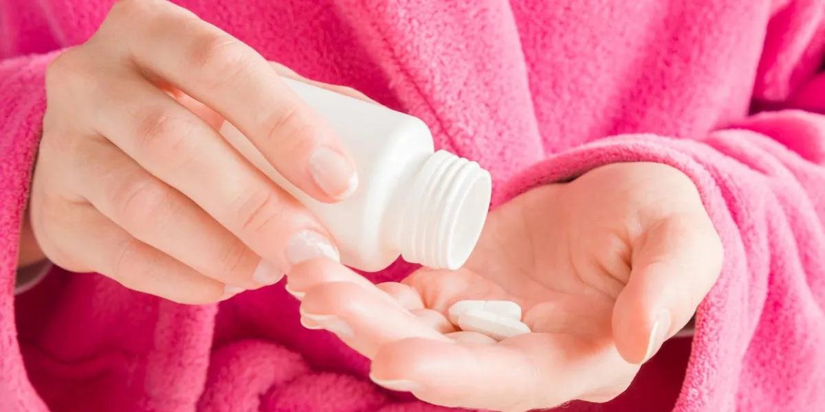 girl in pink bathrobe hands holding a white bottle and pills receiving vitamins or medicaments women's issues medical, pharmacy and healthcare concept