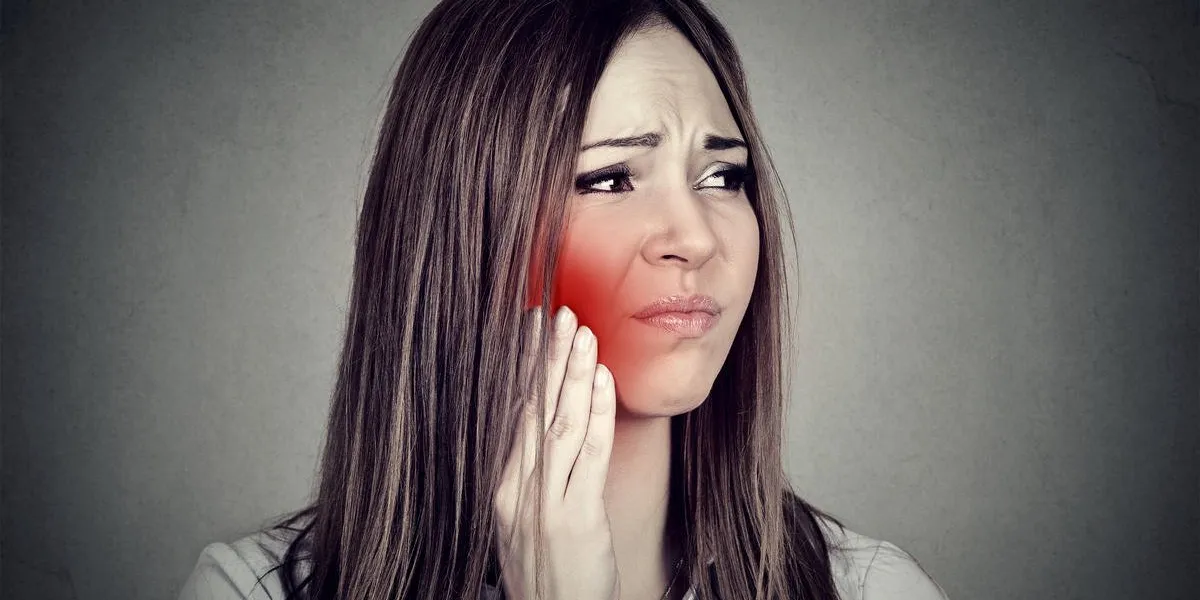 young woman with sensitive toothache crown problem suffering from pain touching outside mouth with hand isolated on gray background negative human emotion feelingn