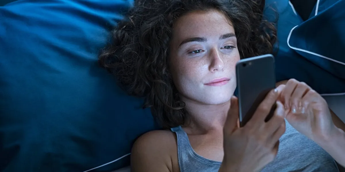 girl awake in bed using cellphone at night