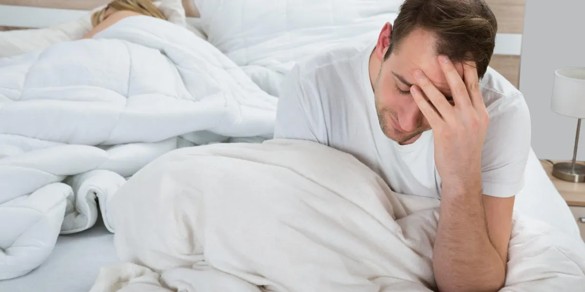 homme déprimé assis sur le lit pendant que la femme dort dans la chambre