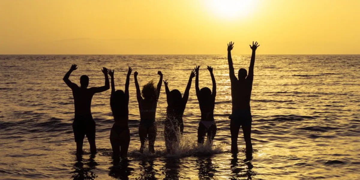 happy friends jumping inside water on the beach at sunset young people having fun on summer vacation travel, party and friendship concept image