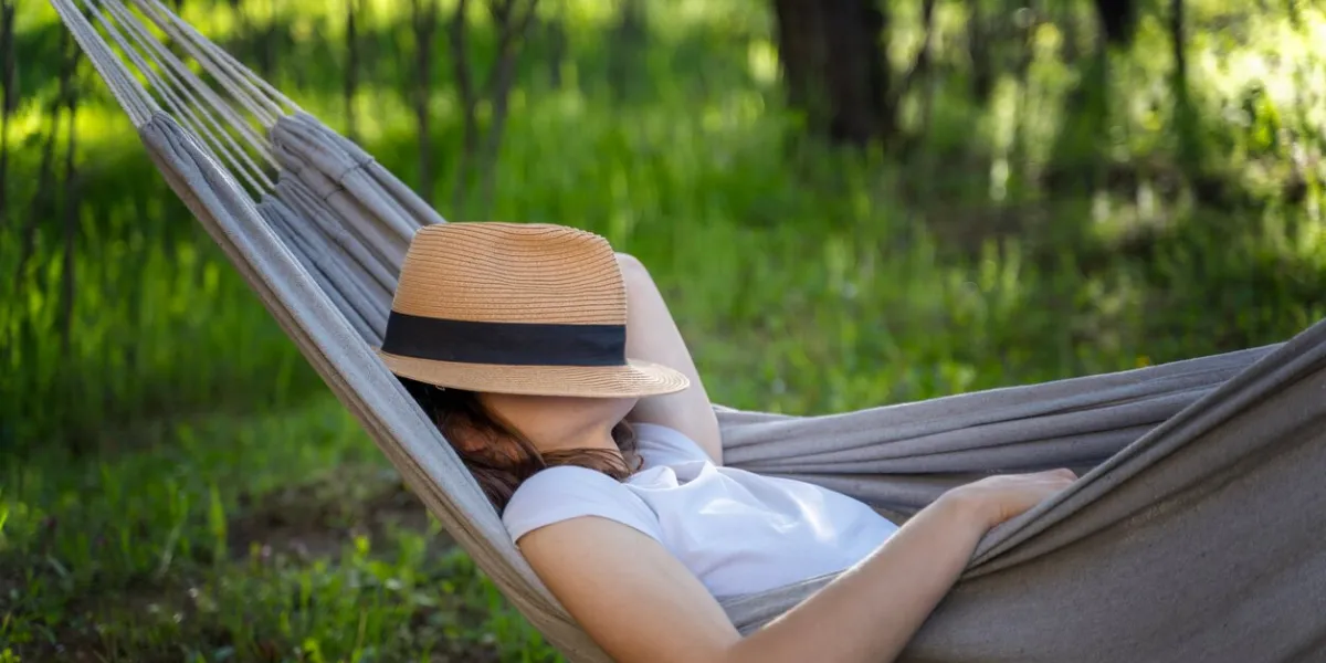 woman resting in a hammock in a summer garden covering her face with a straw hat summer vacation concept